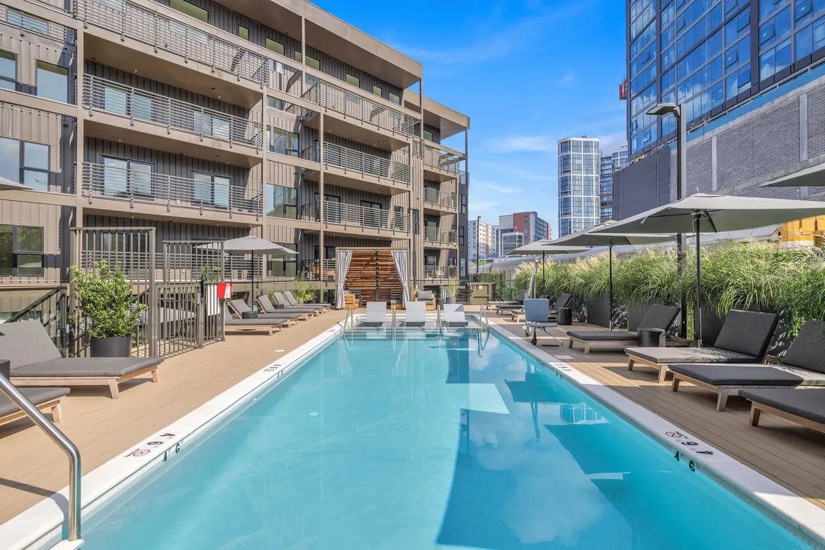 An outdoor pool area with lounge chairs, green grass, wooden deck, and planters. The tranquil setting invites families to relax, sunbathe, and enjoy poolside activities during their stay.