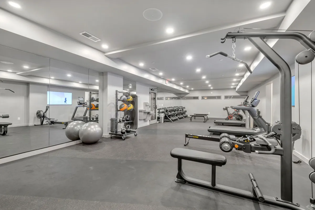 A modern, well-equipped gym interior featuring a variety of exercise equipment, including treadmills, weights, and mirrors, in a bright and spacious setting ideal for maintaining fitness routines while traveling.