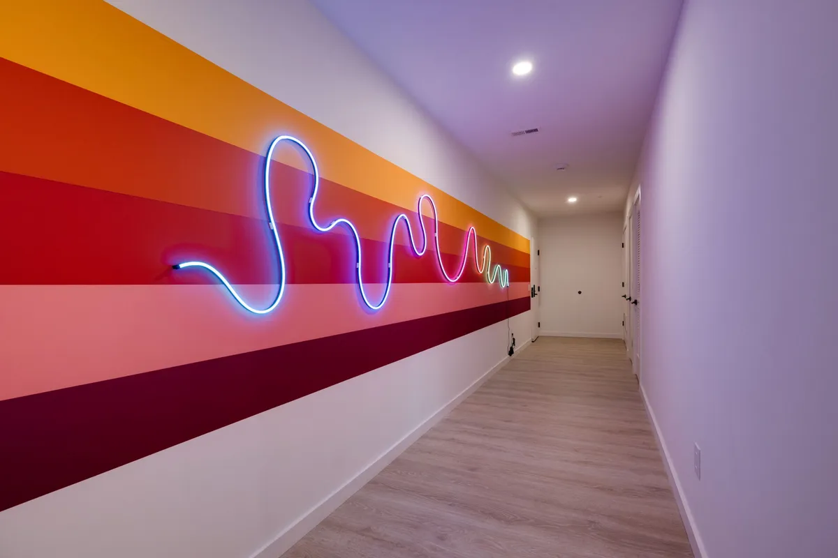 A playful and energetic hallway featuring a neon light installation and a colorful striped wall. The scene is dynamic and visually engaging, representing a memorable passageway that adds excitement to coming and going within the building.