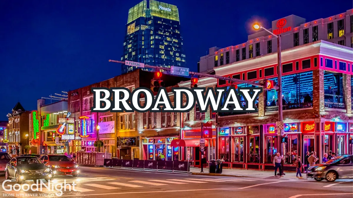 A lively nighttime street scene on Broadway featuring illuminated signs, bustling crowds, and colorful buildings. The area is full of people walking, dining, and enjoying the vibrant nightlife.
