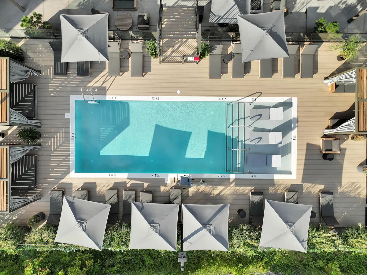 A bright, tranquil swimming pool area with lounge chairs and umbrellas on a spacious deck, perfect for relaxing, sunbathing, or taking a dip. The pool is surrounded by modern decking and offers a leisurely atmosphere for residents.