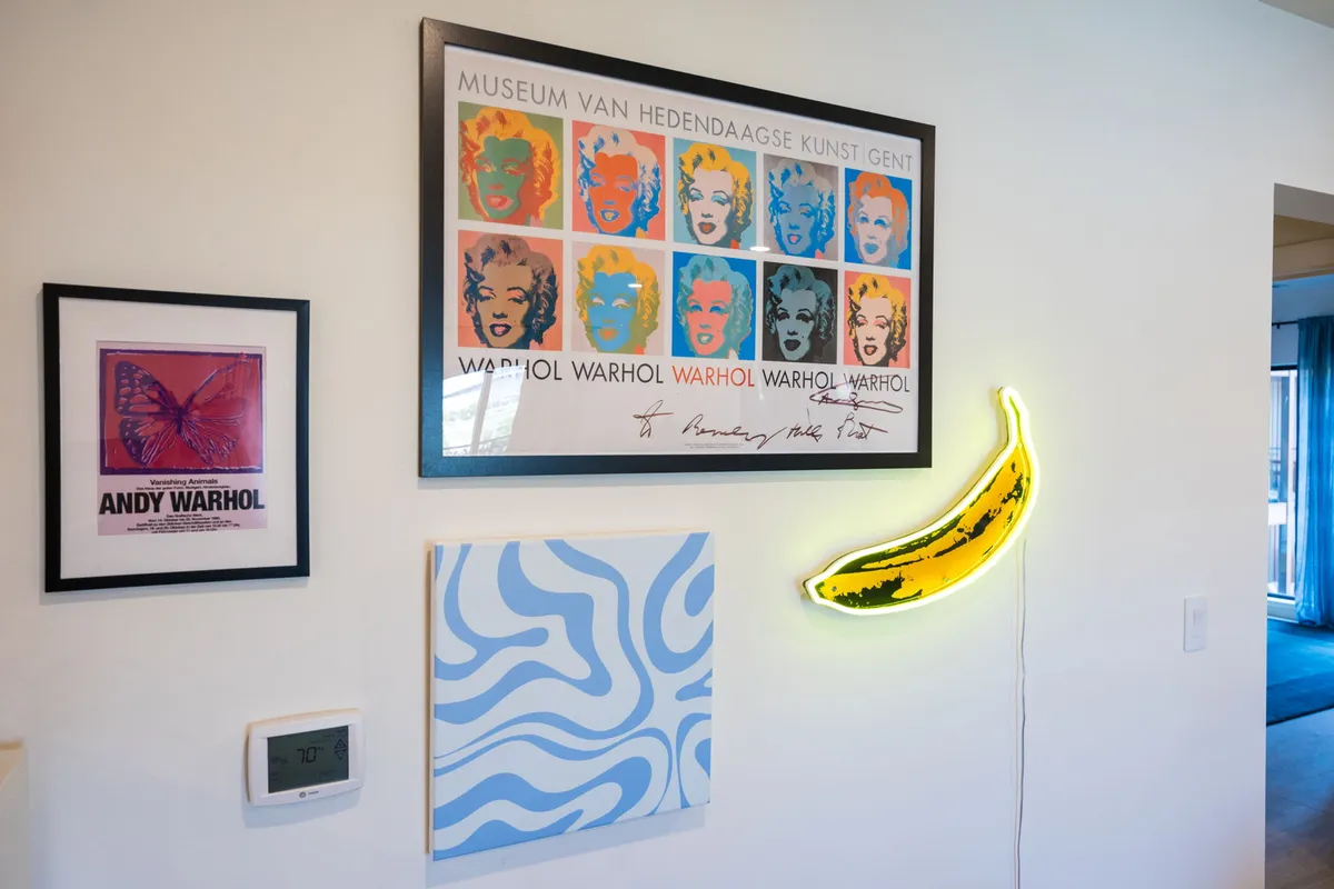 A lively interior scene featuring an Andy Warhol poster, a neon banana light, and an abstract blue wall pattern. The decor is bright, playful, and unmistakably pop art-inspired, capturing the essence of Warhol and modern artistic flair.