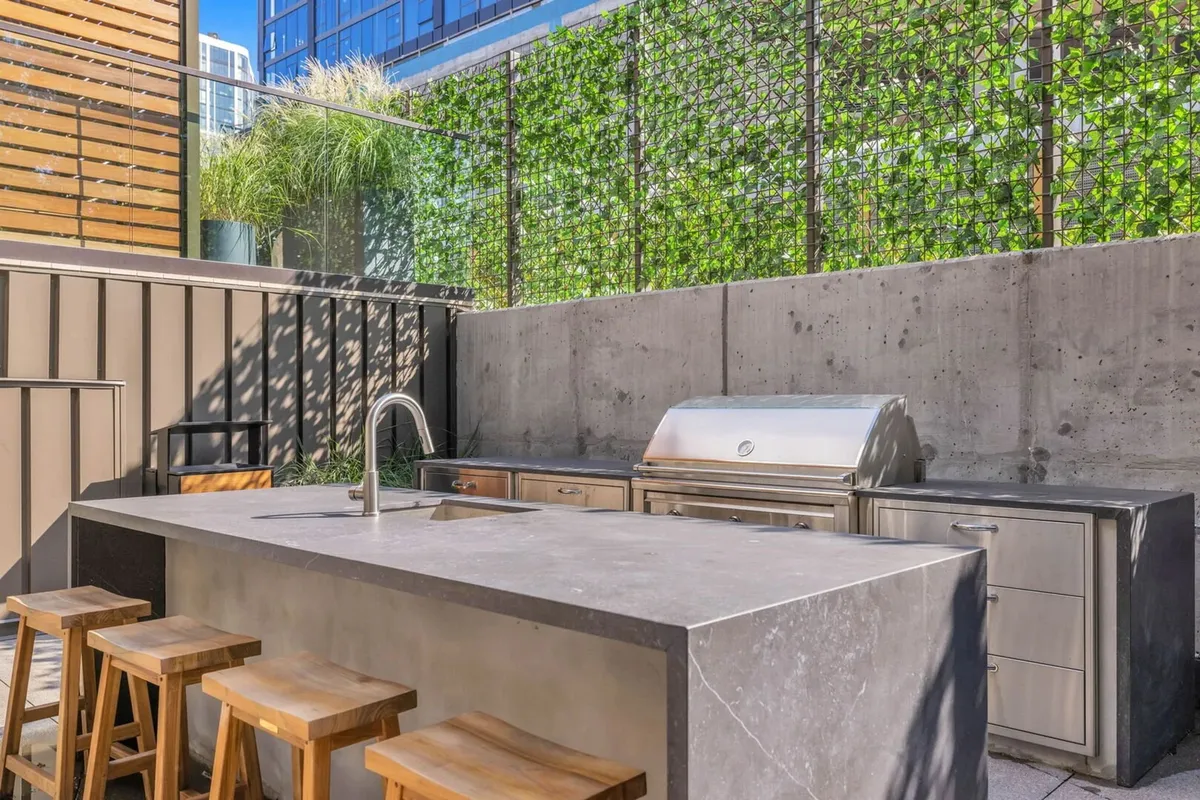 A sophisticated outdoor kitchen and barbecue grill setup, complete with stools and lush green wall, designed for entertaining and communal cooking.