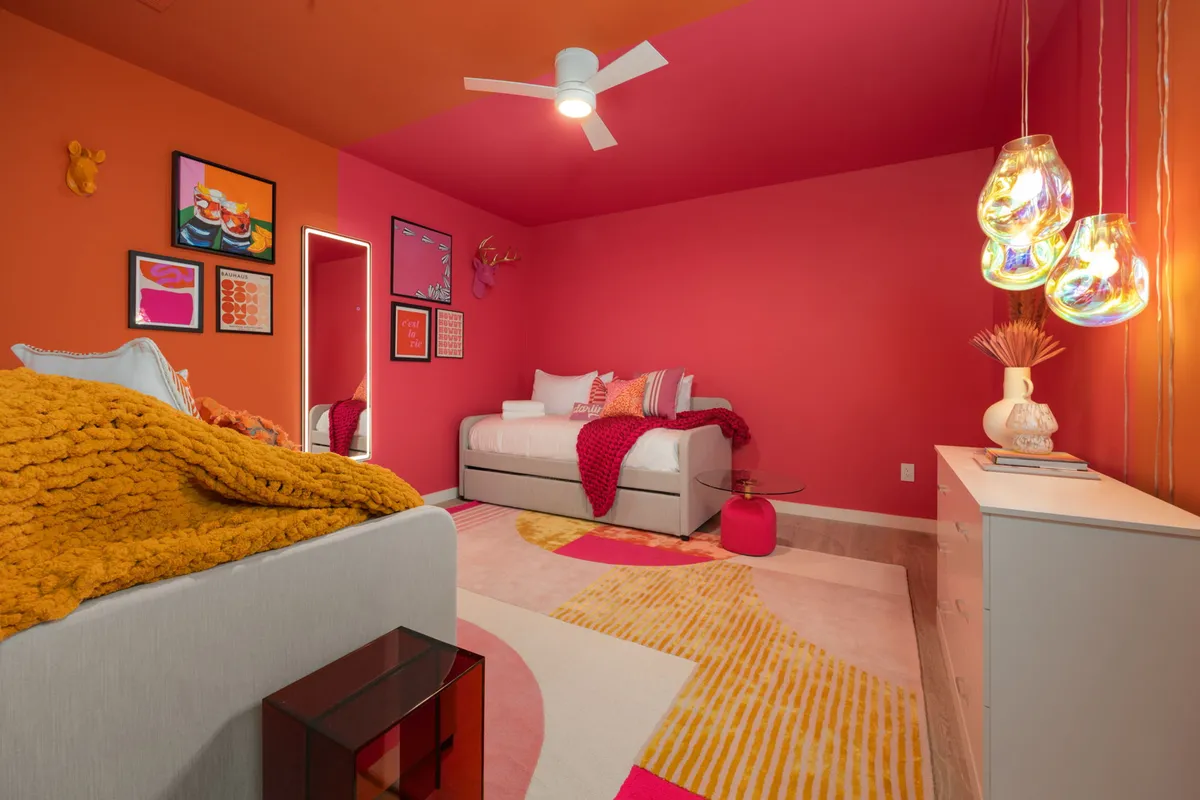 A lively bedroom space with vibrant wall art, brightly colored bedding, stylish ceiling light fixtures, and unique decorative accents. The atmosphere is energetic and creative, ideal for group stays or families.