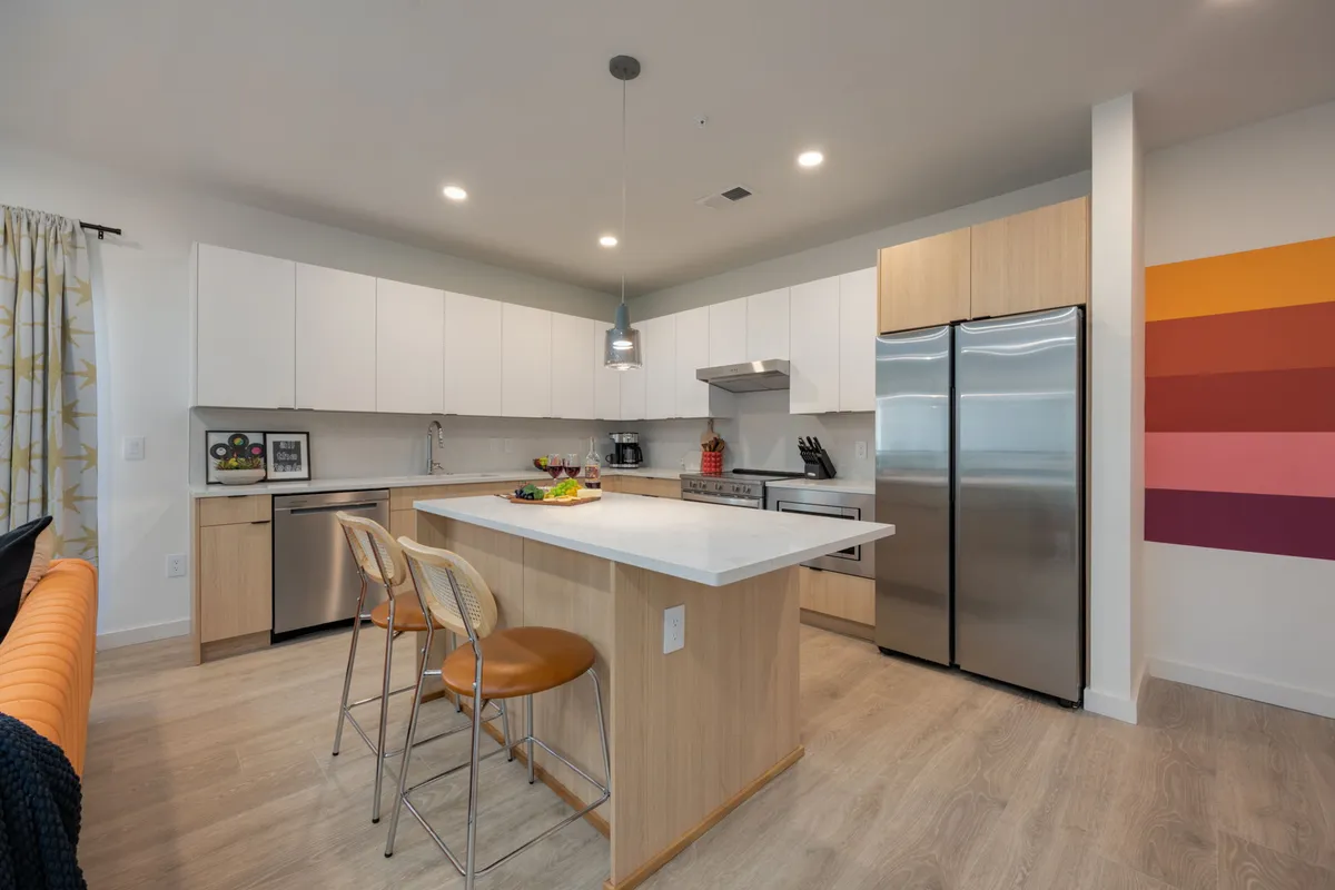 A modern kitchen with a central island, stainless steel appliances, and colorful wall art. The setting feels open and connected, making it perfect for cooking, entertaining, or sharing a meal with friends.