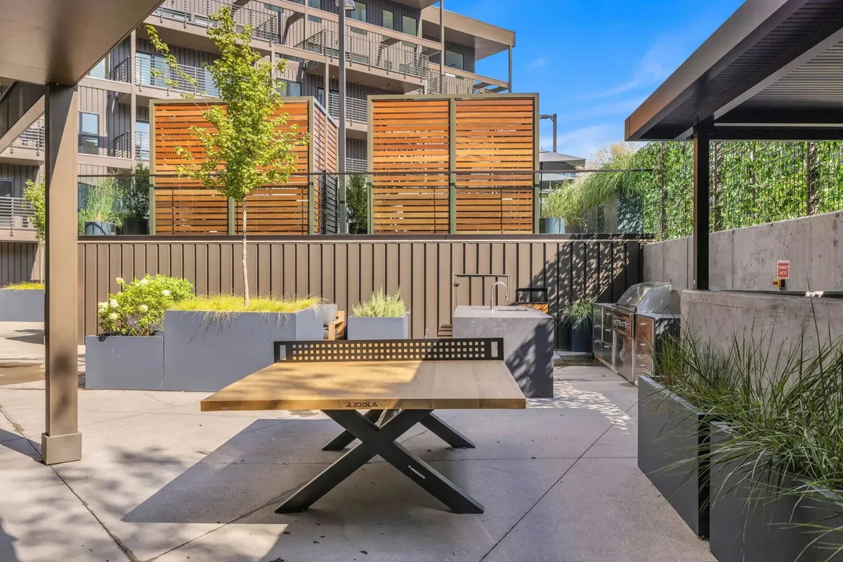 A casual communal grilling and outdoor dining area complete with a wooden table, planters, privacy screens, and open-air ambiance. Designed for group gatherings, it offers an inviting space to enjoy fresh air and meals together.